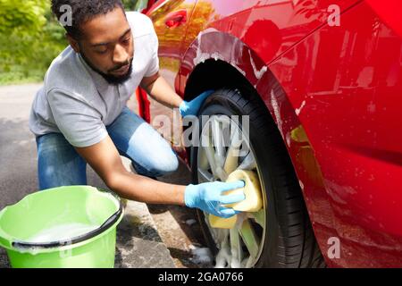Man Washing Wheels Of Car During Valet Using Bucket And Sponge Stock Photo