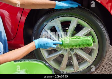 Close Up Of Man Washing Wheels Of Car During Valet Using Bucket And Sponge Stock Photo