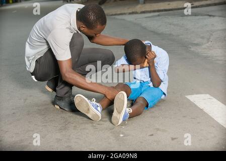 Father comforting his son crying, child fallen on the road having a knee injury Stock Photo