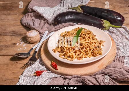 Traditional Sicilian pasta dish of sauteed eggplant topped with tomato sauce. Food served on a ceramic plate, Italian cuisine, modern hard light, dark Stock Photo