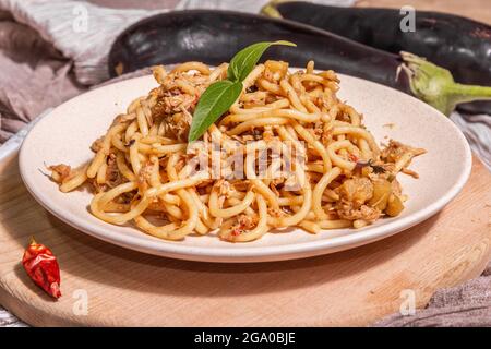 Traditional Sicilian pasta dish of sauteed eggplant topped with tomato sauce. Food served on a ceramic plate, Italian cuisine, modern hard light, dark Stock Photo