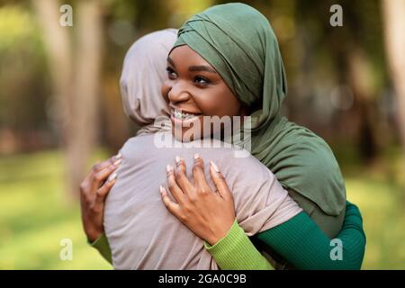 Two Diverse Islamic Ladies Embracing Standing In Park Outside Stock Photo