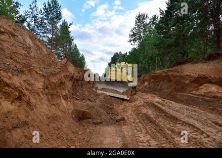 Dozer during clearing forest for construction new road . Yellow Bulldozer at forestry work Earth-moving equipment at road work, land clearing, grading Stock Photo