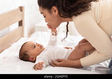 African Mommy Kissing Baby's Hand Waking Up After Sleep Indoor Stock Photo