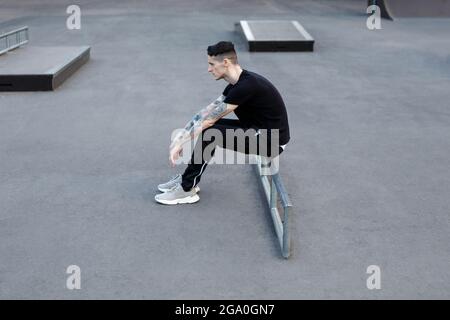 young brunette man sitting alone on an asphalt skate playground Stock Photo