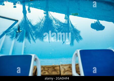 Closeup sunloungers and beautiful swimming pool with reflected of palm trees in a blue water, Egypt. Stock Photo