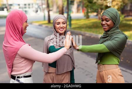 Three Diverse Islamic Women Giving High-Five Standing Outside, Wearing Hijab Stock Photo