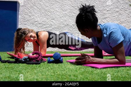 Cheerful diverse female friends doing elbow plank exercise during abs workout while training together in yard of house Stock Photo