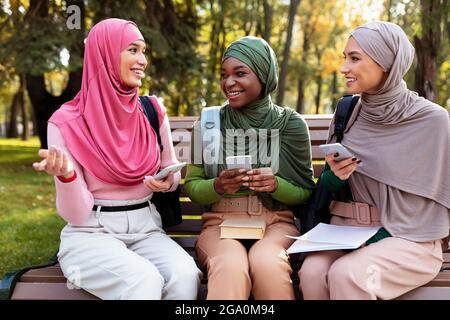 Muslim Women Using Phones Talking And Having Fun In Park Stock Photo