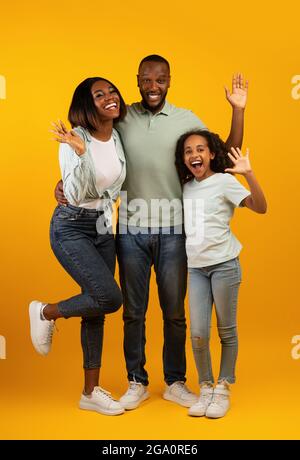 Family concept. Happy african american man, woman and girl waving hands to camera and smiling over yellow background Stock Photo