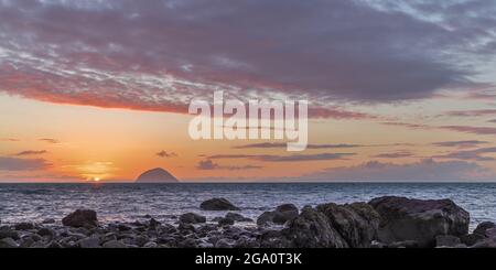 Sunset over the Irish Sea and Ailsa Craig taken from Lendalfoot, South Ayrshire, Scotland with rocks in the foreground Stock Photo