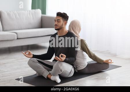 Young Middle Eastern Spouses Meditating Together On Mat In Living Room Stock Photo