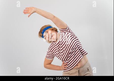 Elderly woman doing fitness doing side bends on a white background. Stock Photo