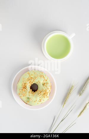 Minimalistic flat lay with cup of green matcha tea, pistachio donut and three wheel of rye Stock Photo