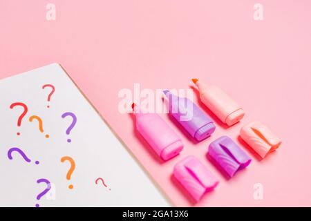 Copybook with question marks and opened multicolored markers on pink background. Close up. Concept of education and creativity. Stock Photo