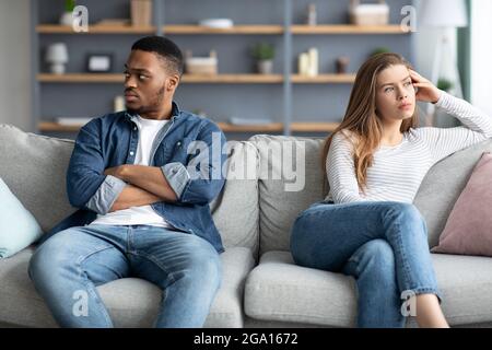 Relationship Crisis. Offended Interracial Couple Sitting On Couch After Quarrel Stock Photo
