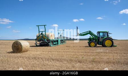 Tractor with bale spike on a stubble field loading bales of straw Stock Photo