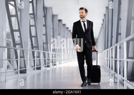 Middle-aged businessman walking by airport terminal, carrying luggage Stock Photo