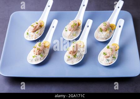 Cold appetizer made from cod liver, cod caviar, olives, cucumber and microgreens on serving spoons. Traditional cold dish. Close-up, blue plate, black Stock Photo