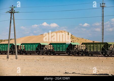 Altynkol, Kazakhstan - June 05, 2012: Railway station Altynkol. Hopper cars train on yellow sand dune and blue sky with clouds backdrop. Stock Photo