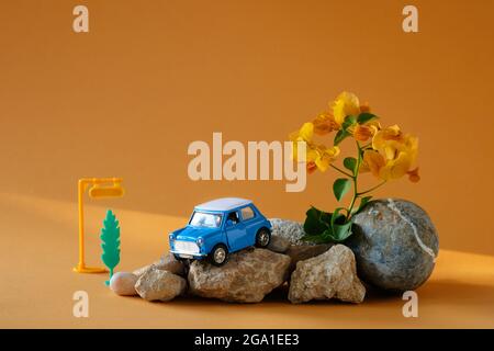 Blue toy car on stones and orange background like a symbol of road trips.Travel concept or rent a car. Stock Photo