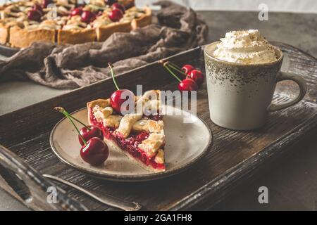 A piece of fresh cherry pie and a cup of coffee with cream on a wooden tray Stock Photo