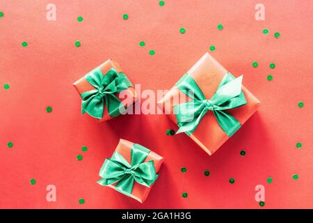 Three gift boxes with green bows and confetti on red background. Christmas concept. Top view, flat lay. Stock Photo