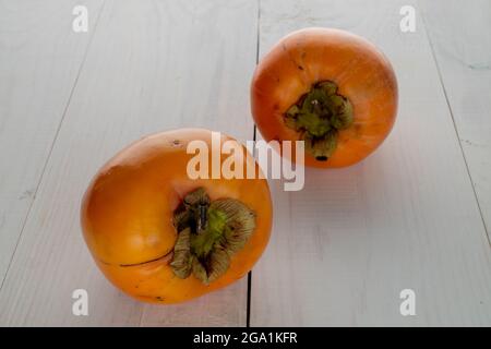 Two ripe yellow persimmons, close-up, on brown paper.