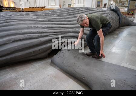 Greifswald, Germany. 28th July, 2021. Gil Shachar, an artist from Isarel, is setting up a whale sculpture of a humpback whale in St. Nicholas Cathedral. The 14-metre-long whale sculpture is a cast of an animal washed up in South Africa in 2018. The art project in Greifswald is intended to make people think. On it, for example, bite marks from sharks or also cuts from ship's propellers can be seen. The sculpture has already been exhibited in Berlin and Bochum. Credit: Stefan Sauer/dpa/Alamy Live News Stock Photo