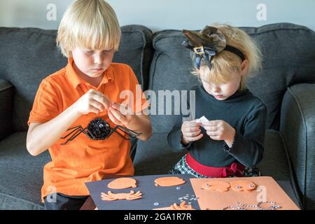 Halloween kids craft preparations. Little children doing crafts at home. Halloween family party concept. Stock Photo