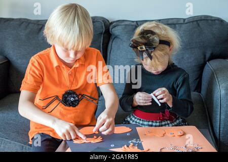 Little children doing Halloween crafts at home, wearing holiday costumes Stock Photo