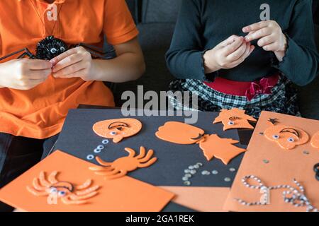 Halloween kids craft preparations. Little children doing crafts at home. Boy and girl wearing black and orange clothes, sitting at the table, maiking Stock Photo
