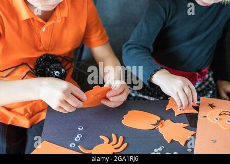 Halloween kids craft preparations. Little children doing crafts at home. Brother and sister wearing orange and black, making spiders for the holiday p Stock Photo