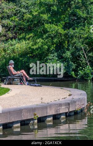 man sitting at the edge of the bridgewater canal in greater manchester on the riverbank towpath fishing angling relaxing on a sunny day. Stock Photo