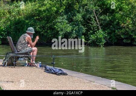 man sitting at the edge of the bridgewater canal in greater manchester on the riverbank towpath fishing angling relaxing on a sunny day. Stock Photo