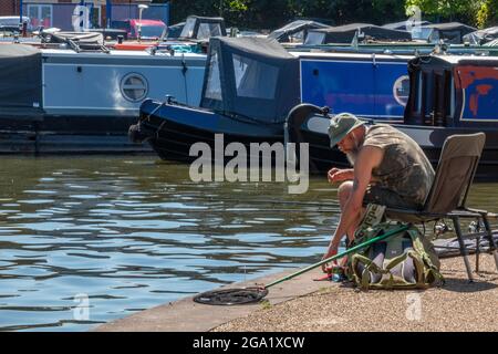 middle-aged older man fishing at the side of the bridgewater canal in manchester. man fishing a canal next to some narrowboats and craft on the canal. Stock Photo