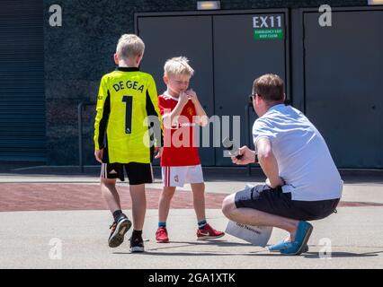 manchester united football shirts being worn by two small boys with proud sporting father supporter and fan taking a photograph of his kids with phone