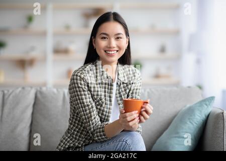 Cheerful asian lady drinking coffee in living room Stock Photo