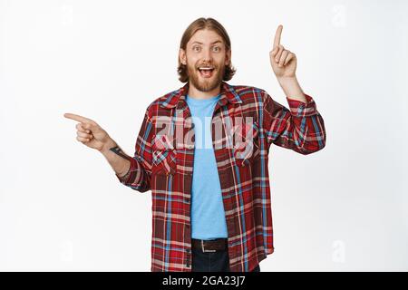 Image of happy blond guy, laughing and smiling while showing left and up promo deals, sale banners sideways, two choices, standing against white Stock Photo