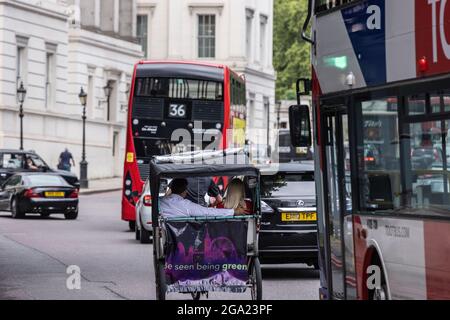 A couple take a ride and dodge the rush hour traffic in a cycle rickshaw taxi, Hyde park Corner, London, England, United Kingdom Stock Photo