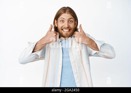 Sounds good. Funny blond guy smiling, showing thumbs up in approval, like great choice, support you, praise great idea, standing satisfied against Stock Photo
