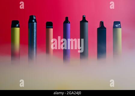 multicolored vape electronic cigarettes on a red background in the smoke Stock Photo