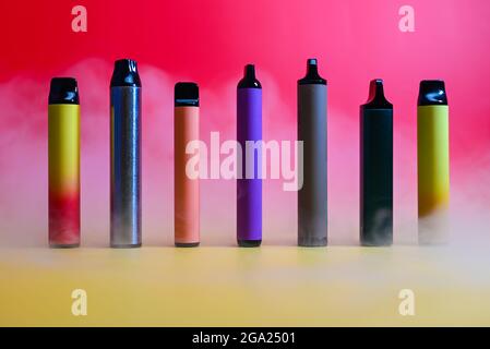 multicolored vape electronic cigarettes on a red background in the smoke Stock Photo