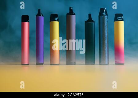 multicolored vape electronic cigarettes on dark green background in smoke Stock Photo