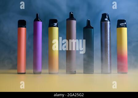 multicolored vape electronic cigarettes on dark green background in smoke Stock Photo