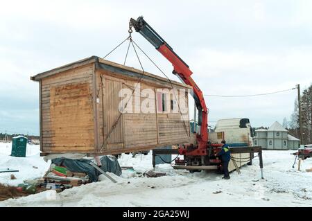 LENINGRAD REGION, RUSSIA - MARCH 04, 2021: A truck with a crane manipulator loads a construction house on the construction site of a country house Stock Photo