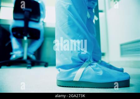 The legs and feet of a researcher standing in a laboratory doing work with a blue cleanroom suit; Germany Stock Photo