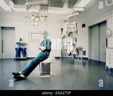 Surgeon sits in scrubs and surgical cap inside an operating room; Germany Stock Photo