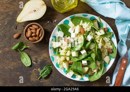 Autumn fruit salad. Couscous salad with pear, spinach, feta cheese and vinaigrette sauce on a wooden rustic table. Top view flat lay background. Stock Photo