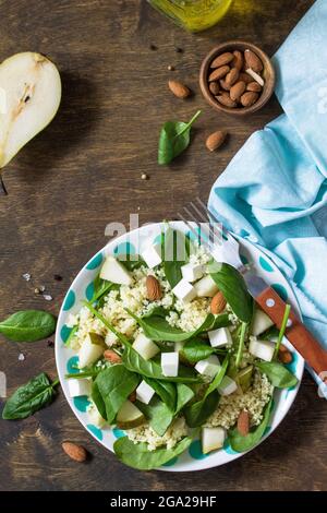 Autumn fruit salad. Couscous salad with pear, spinach, feta cheese and vinaigrette sauce on a wooden rustic table. Top view flat lay background. Copy Stock Photo